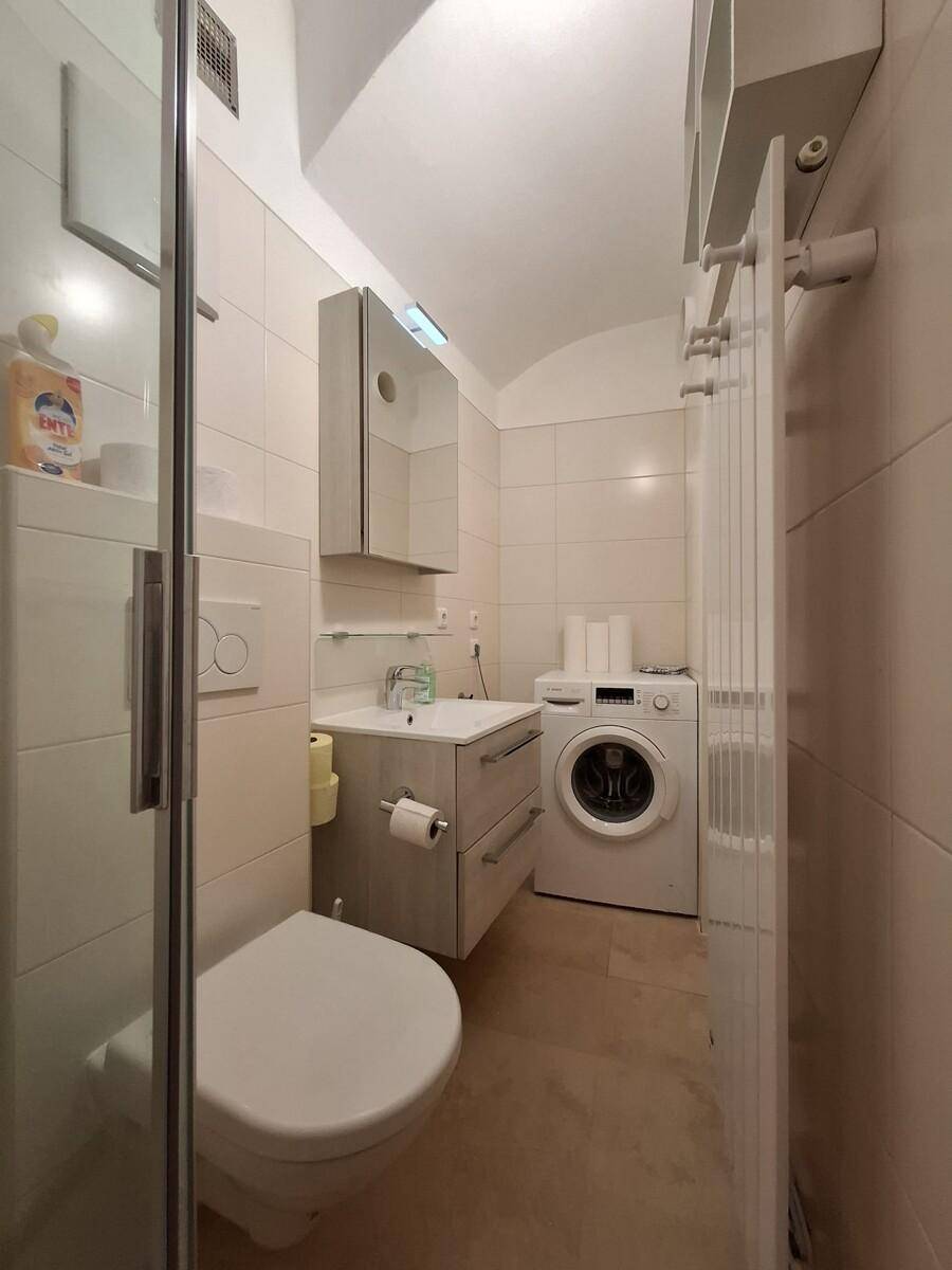 Funktionales Badezimmer mit Dusche, Waschmaschine und praktischem Stauraum.