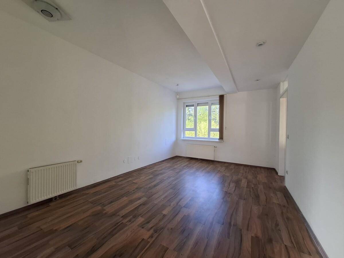 Heller Wohnbereich mit Holzboden und Fenster, das einen Blick ins Grüne bietet.