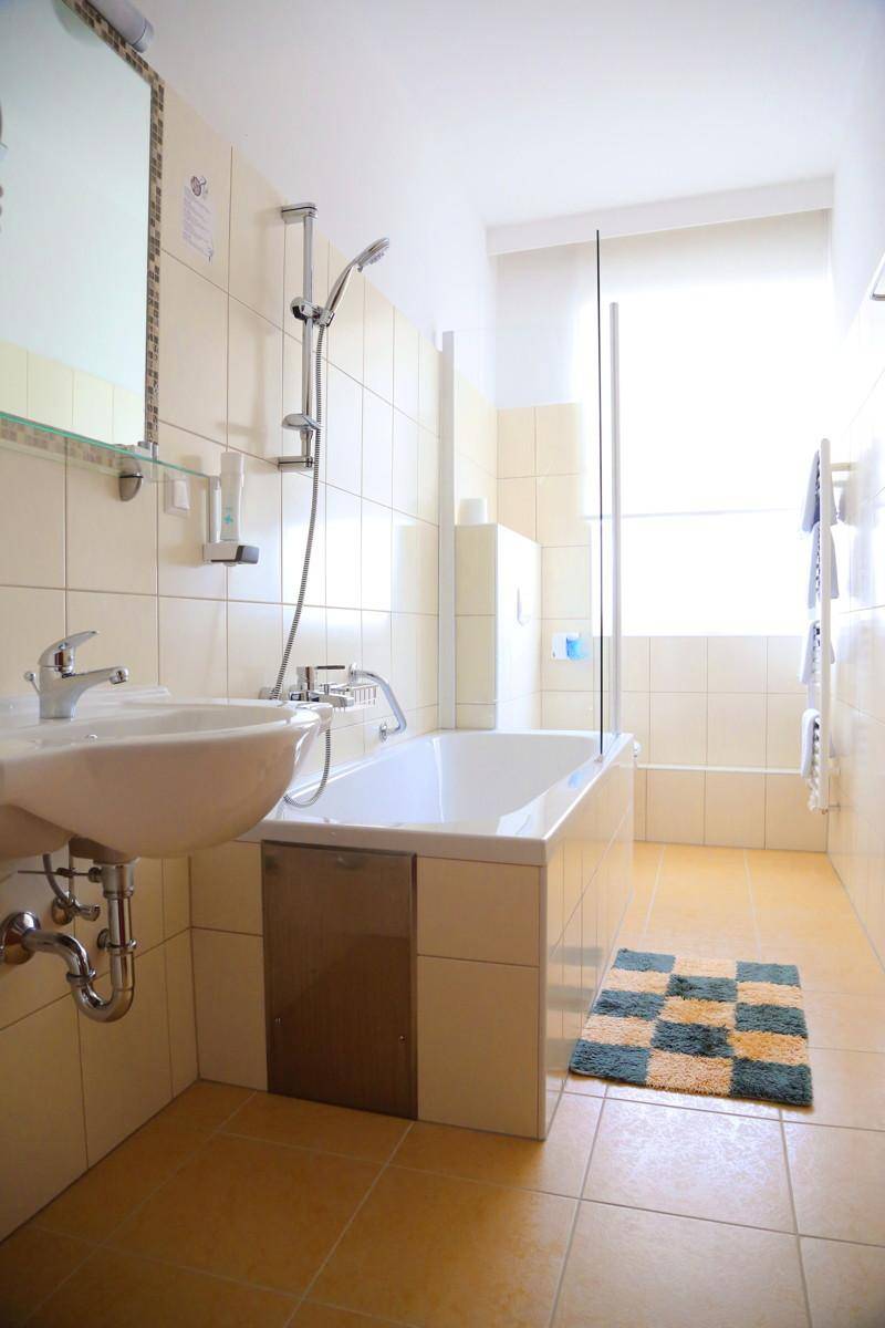 Helles Badezimmer mit Badewanne, Dusche und beigefarbenen Fliesen.