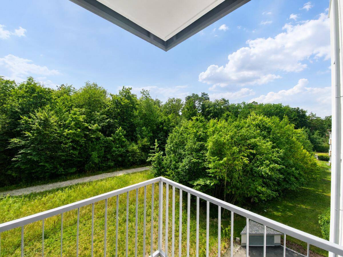 Heller Balkon mit weitem Blick ins Grüne und blauen Himmel.