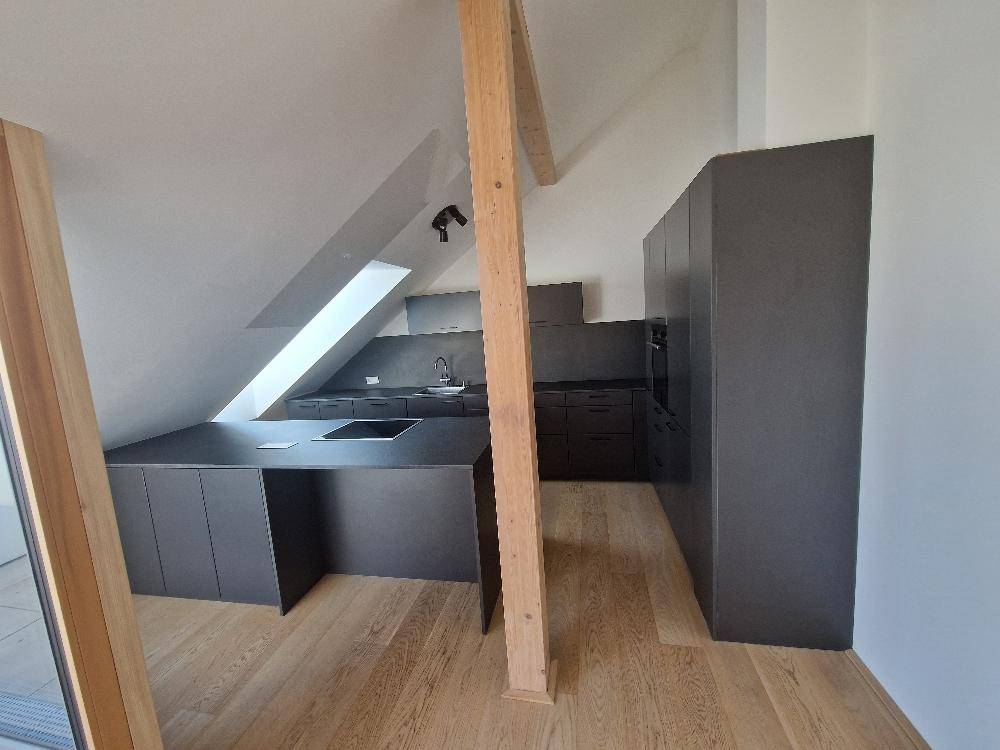 Moderne Küche im Dachgeschoss mit dunklen Schränken, Kochinsel und Holzbalken.