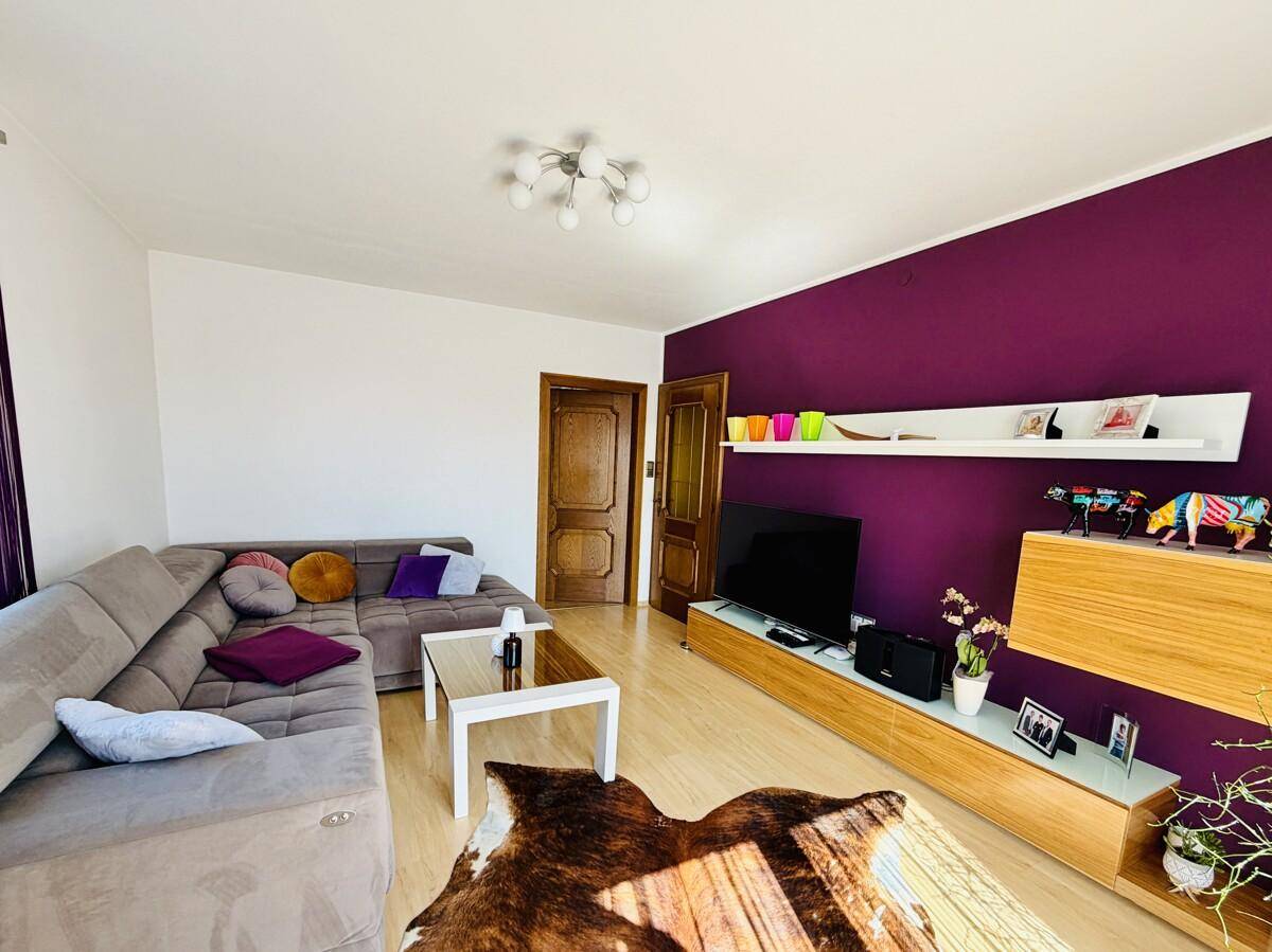 Geräumiges Wohnzimmer mit lila Akzentwand, TV-Möbel und gemütlicher Sitzecke.