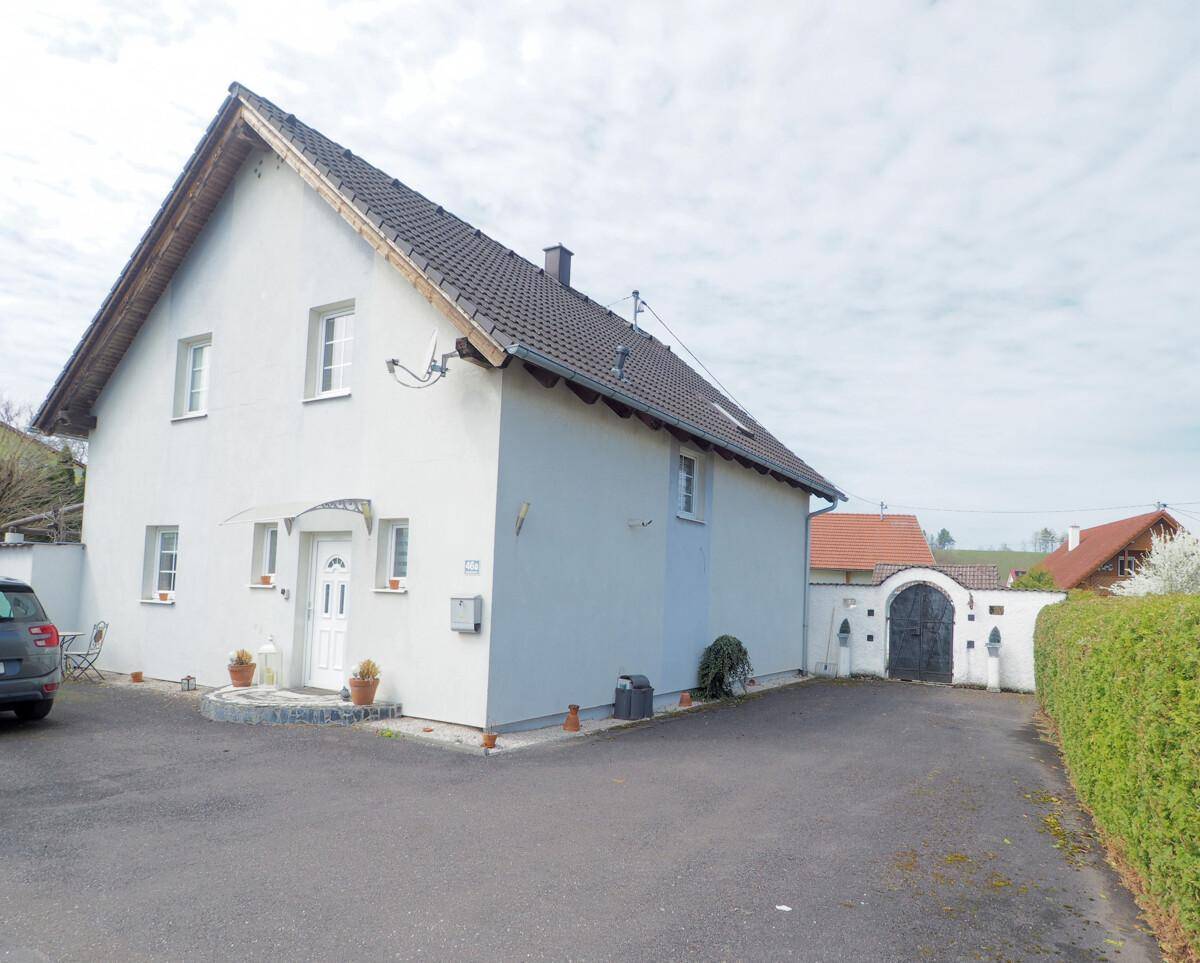 Vorderansicht des Hauses mit Einfahrt, Parkplatz und einem gepflegten Vorgartenbereich.