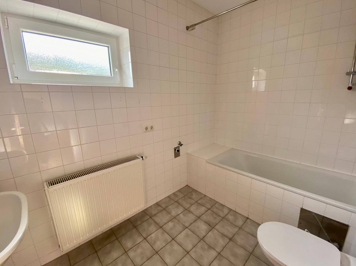 Funktionales Badezimmer mit weißen Fliesen, Badewanne und Fenster für Tageslicht.