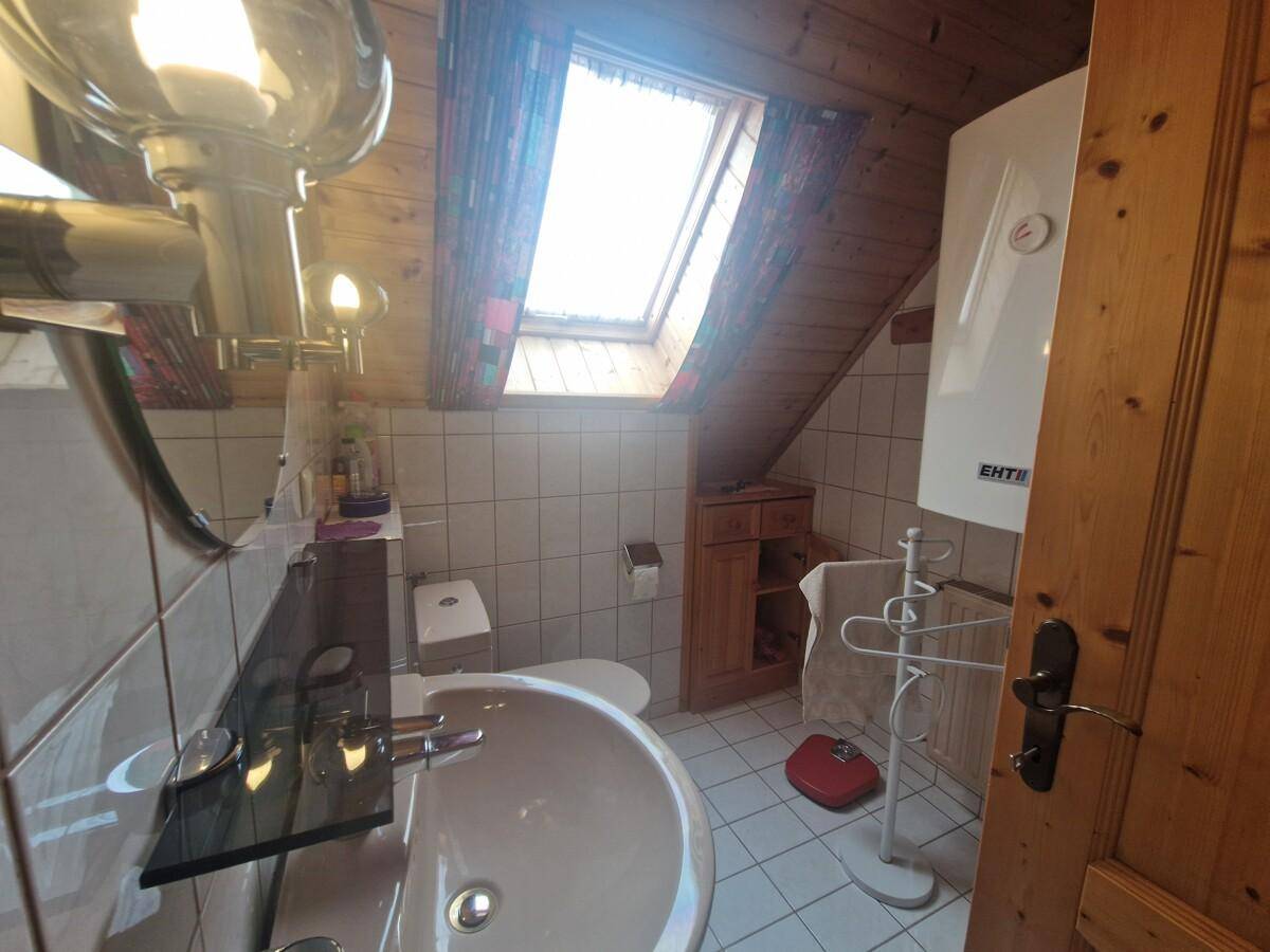 Dachgeschoss-Badezimmer mit Dachfenster, Waschbecken und Holzwänden, hell gefliest.