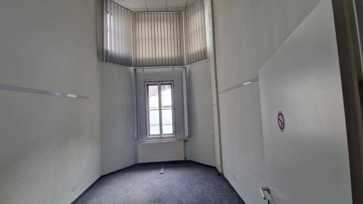 Leerer Büroraum mit Teppichboden und einem Fenster, das durch eine Türöffnung sichtbar ist.