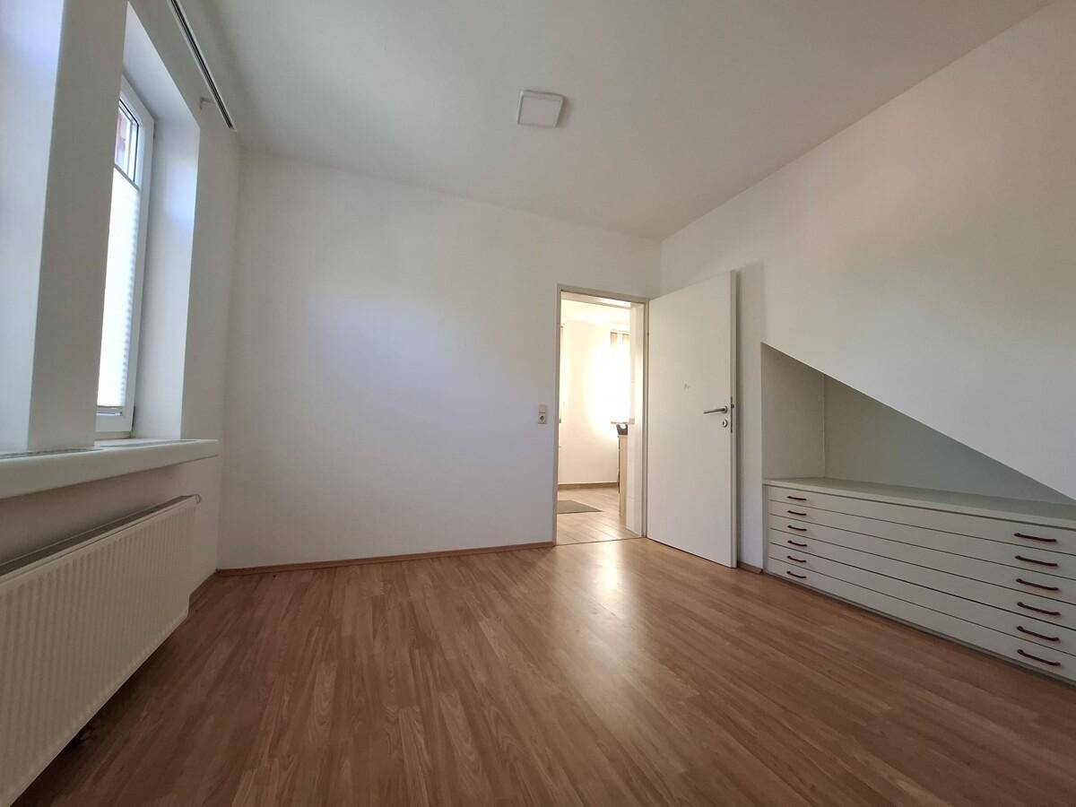 Leeres Schlafzimmer mit Laminatboden, weißen Wänden und einem Einbauschrank unter der Dachschräge.