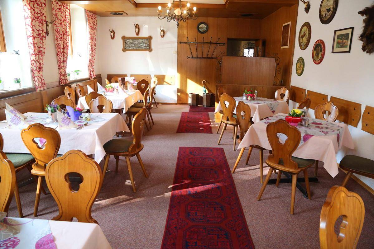 Speisesaal mit Teppichboden, Holztischen und traditioneller Dekoration an den Wänden.