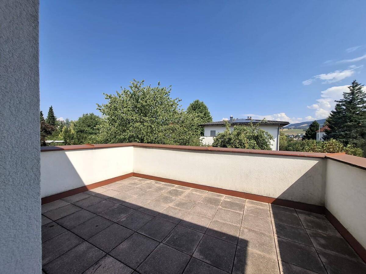 Geräumiger Balkon mit Fliesenboden und Blick ins Grüne unter blauem Himmel.