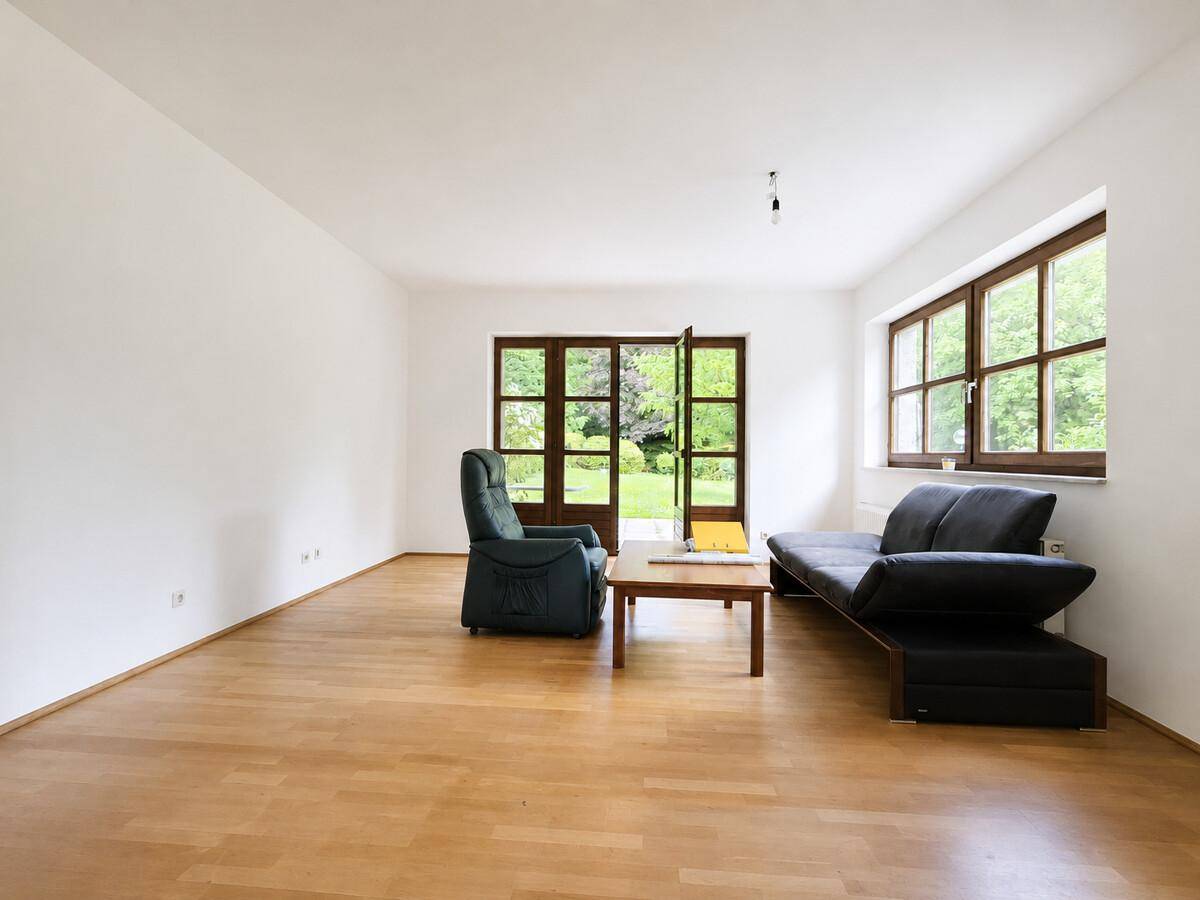 Geräumiges Wohnzimmer mit Holzparkettboden, großen Fenstern und Gartenzugang.