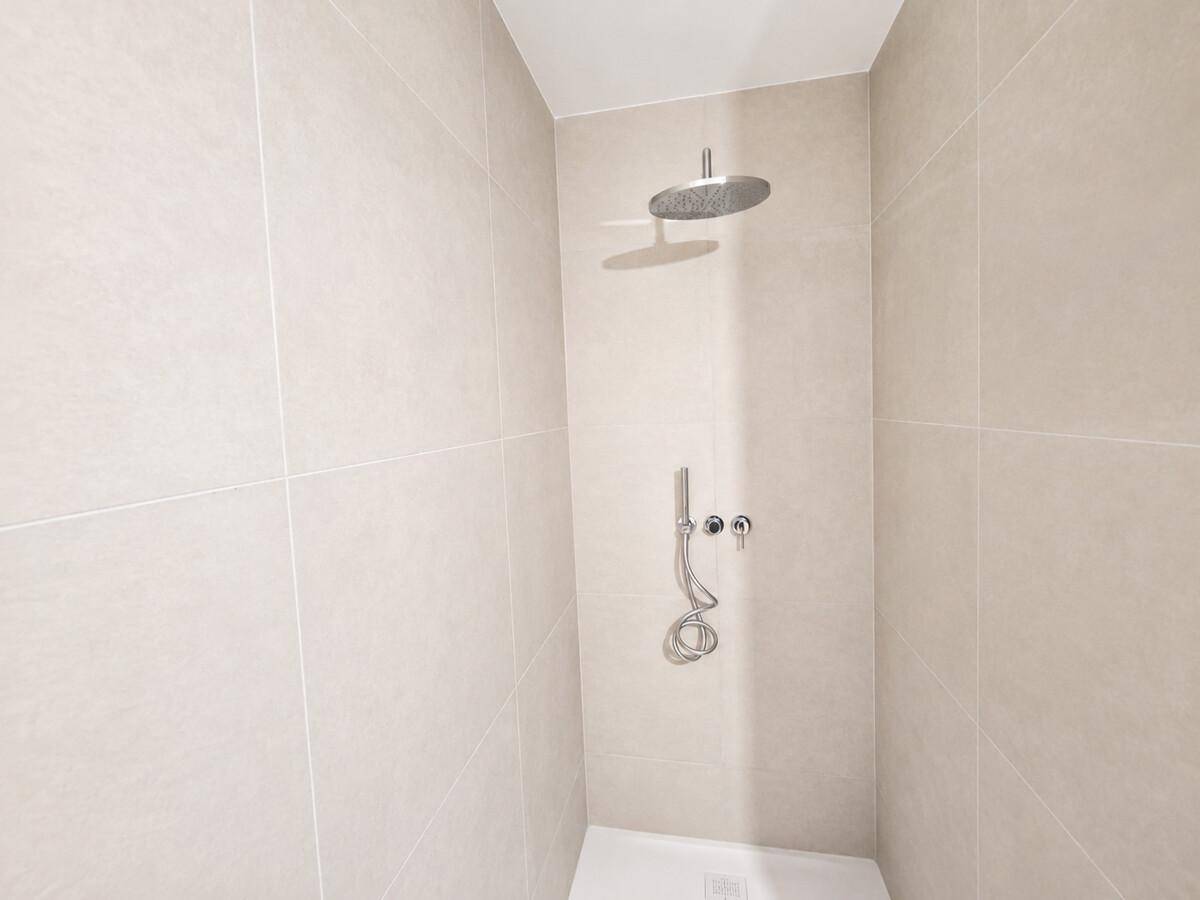 Moderne Duschkabine mit beigefarbenen Fliesen und einer Regendusche.