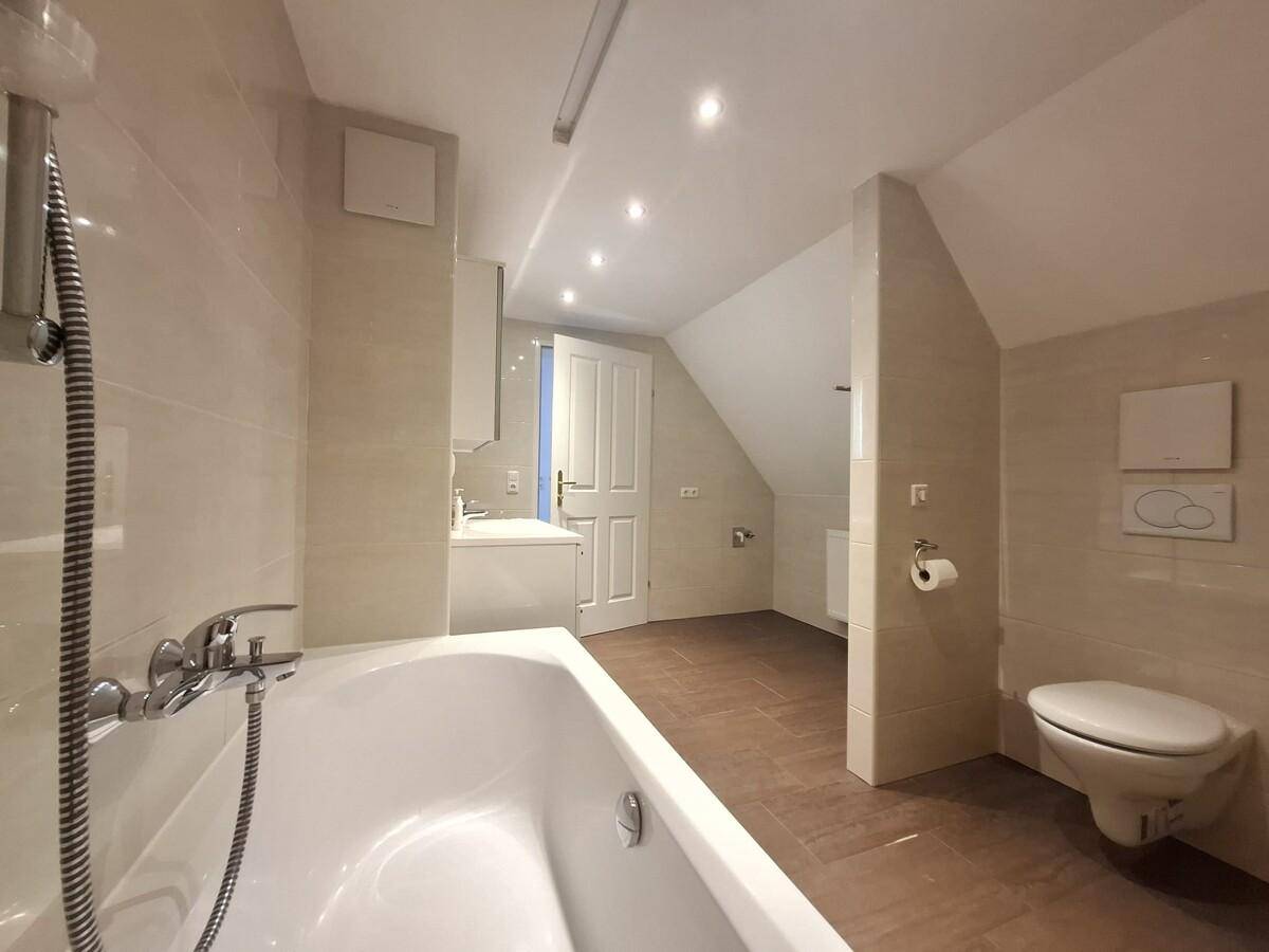 Modernes Badezimmer im Dachgeschoss mit Badewanne, WC und hellen Fliesen.