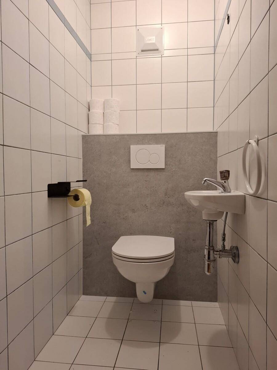 Kleines Gäste-WC mit Wand-WC, Waschbecken und weißen Fliesen.