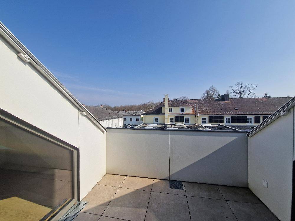 Dachterrasse mit Fliesenboden und Blick auf umliegende Gebäude und Bäume.