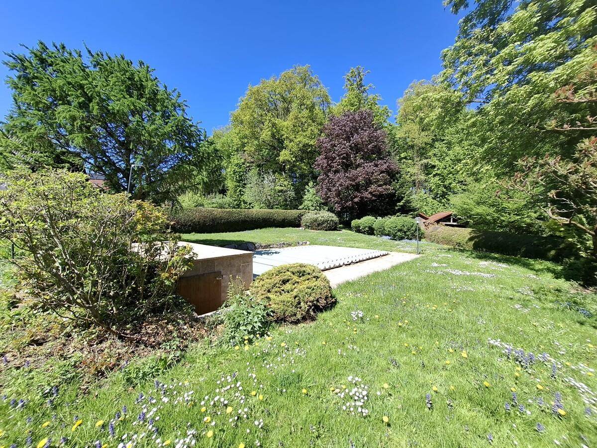 Großer Garten mit viel Grün, Bäumen und einem abgedeckten Poolbereich.