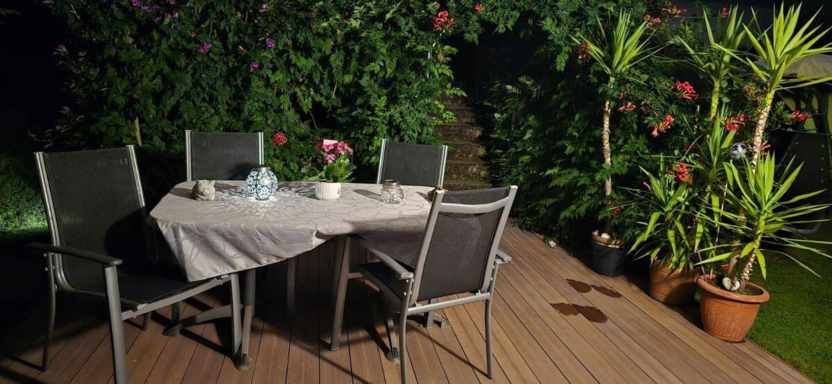 Beleuchtete Holzterrasse am Abend mit Esstisch und Pflanzen für gemütliche Stunden.