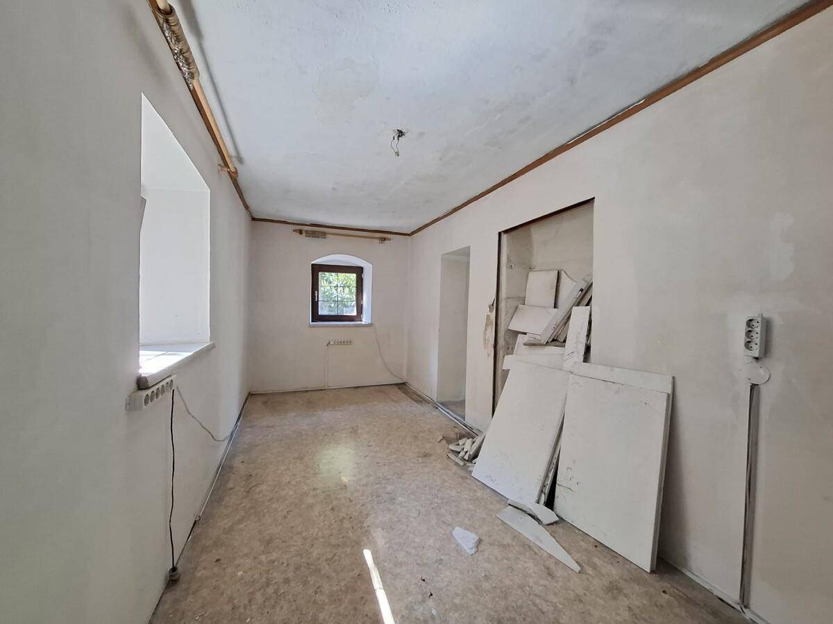 Leerer Raum in Renovierung mit weißen Wänden, einem Fenster und sichtbaren Leitungen.