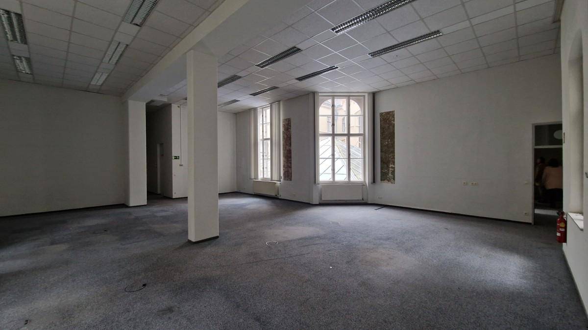 Geräumiger, leerer Bürobereich mit Teppichboden, Säulen und hohen Fenstern, die viel Licht spenden.