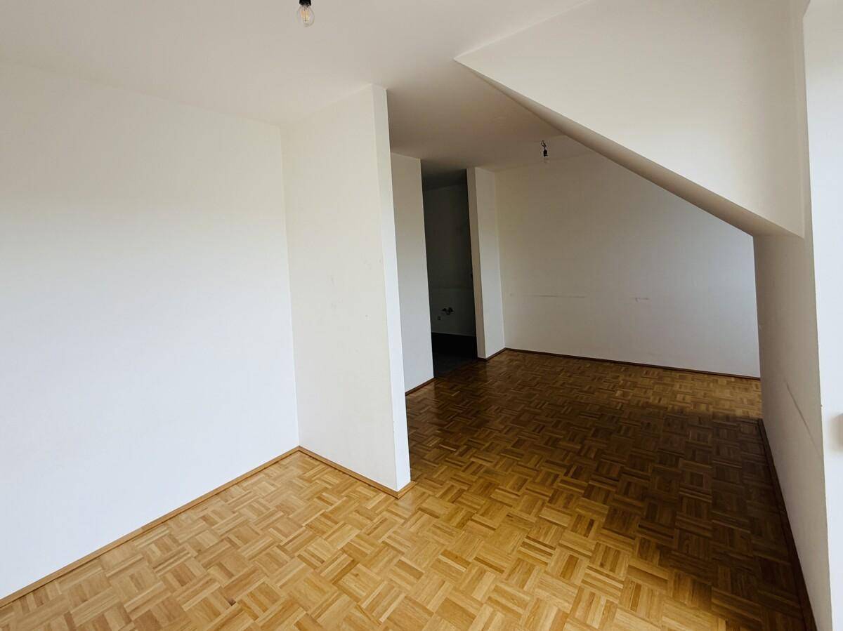 Freundliches Zimmer mit Parkettboden und Dachschräge, bietet Zugang zu einem weiteren Raum.