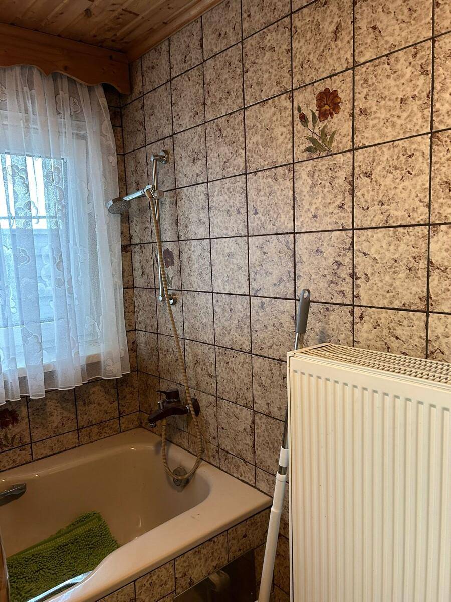 Badezimmer im 80er-Jahre-Stil mit Badewanne, gemusterten Fliesen und Holzdecke.