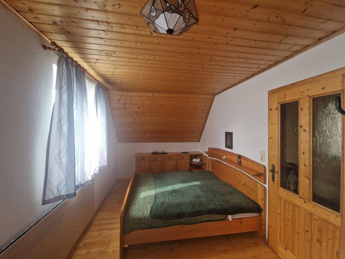 Gemütliches Schlafzimmer im Dachgeschoss mit Holzdecke, Holzbett und Parkettboden.