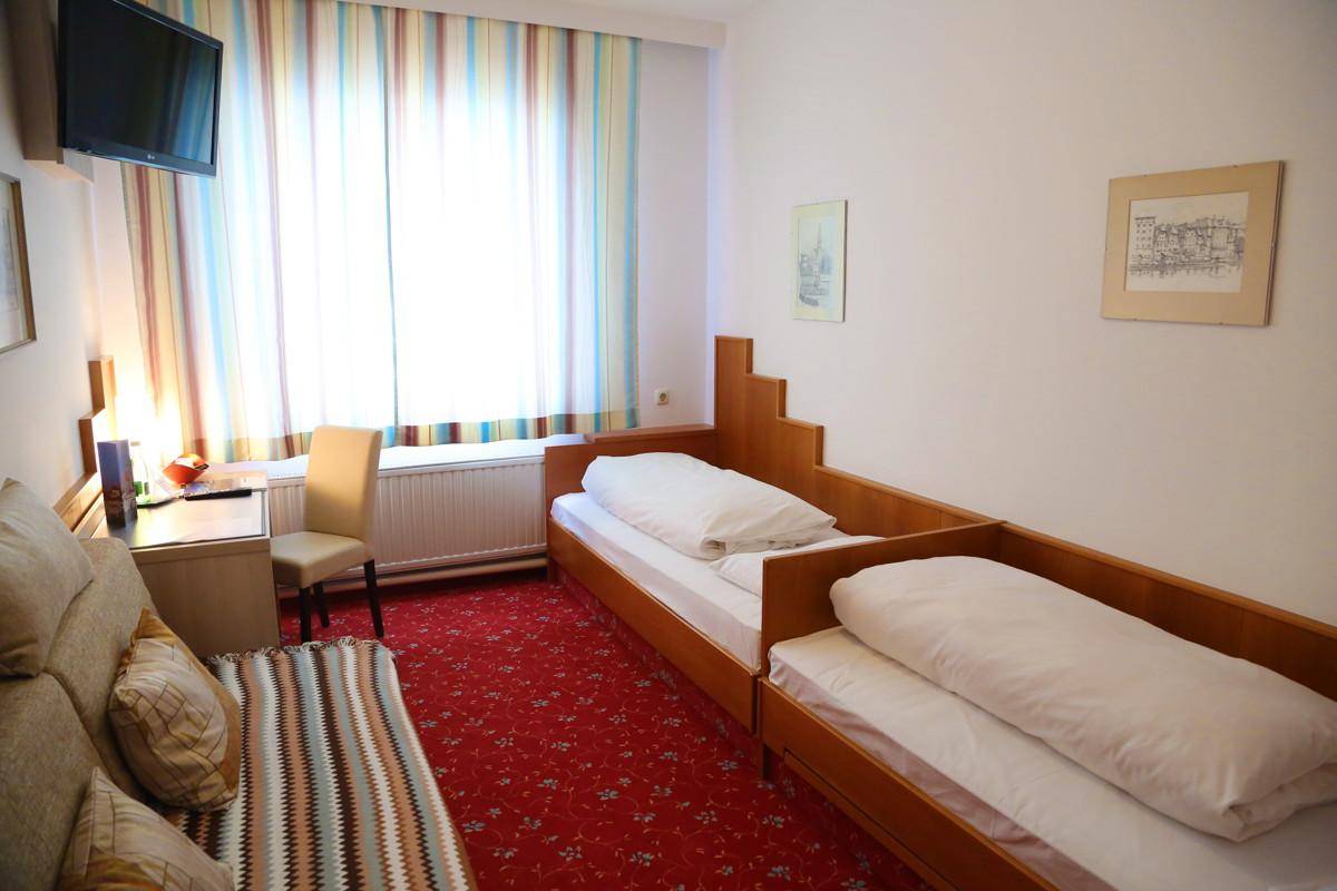 Schlafzimmer mit zwei Einzelbetten, Schreibtisch und rotem Teppichboden.