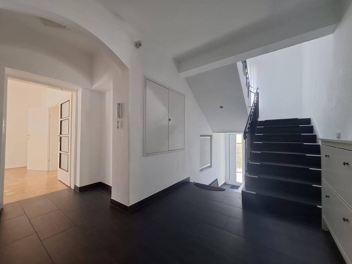 Heller Flur mit Treppe, dunklen Fliesen und Zugang zu weiteren Räumen im Haus.