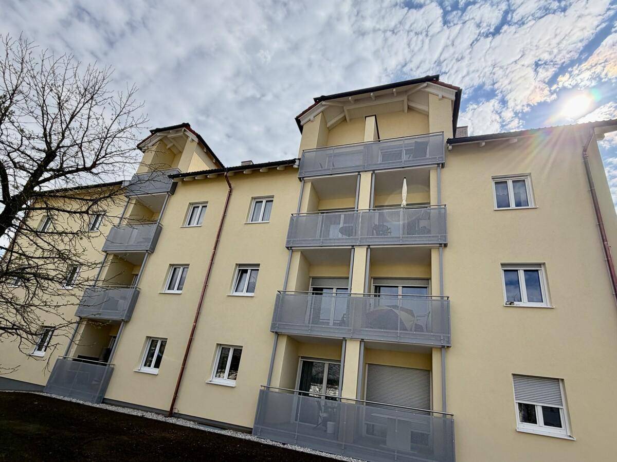 Mehrfamilienhaus mit gelber Fassade, zahlreichen Balkonen und modernen Fenstern unter bewölktem Himmel.