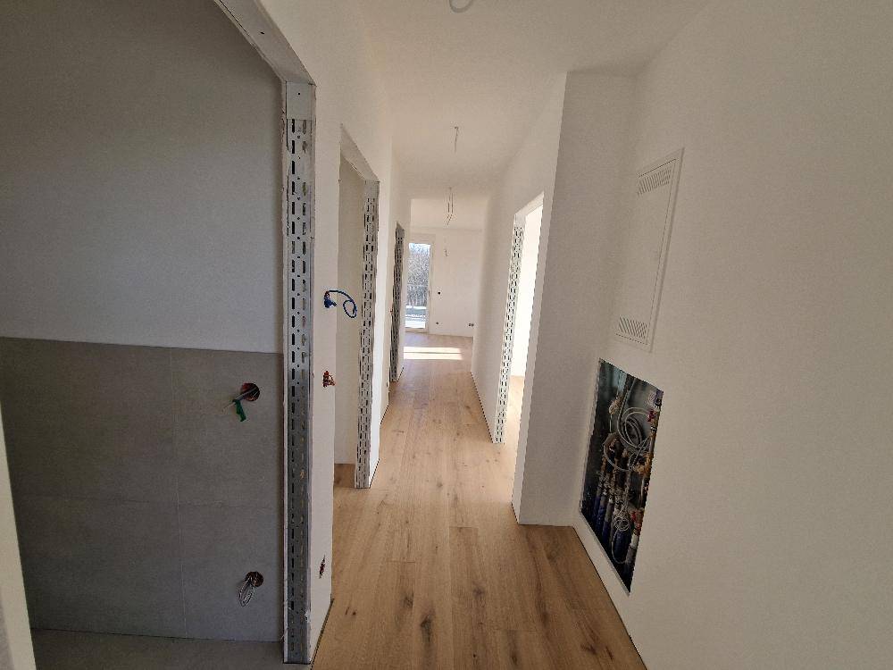 Langer Flur mit Holzboden und weißen Wänden, der verschiedene Räume verbindet.
