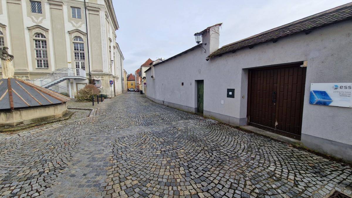 Historische Kopfsteinpflastergasse mit alten Gebäuden und einem großen Holztor an einem grauen Tag.