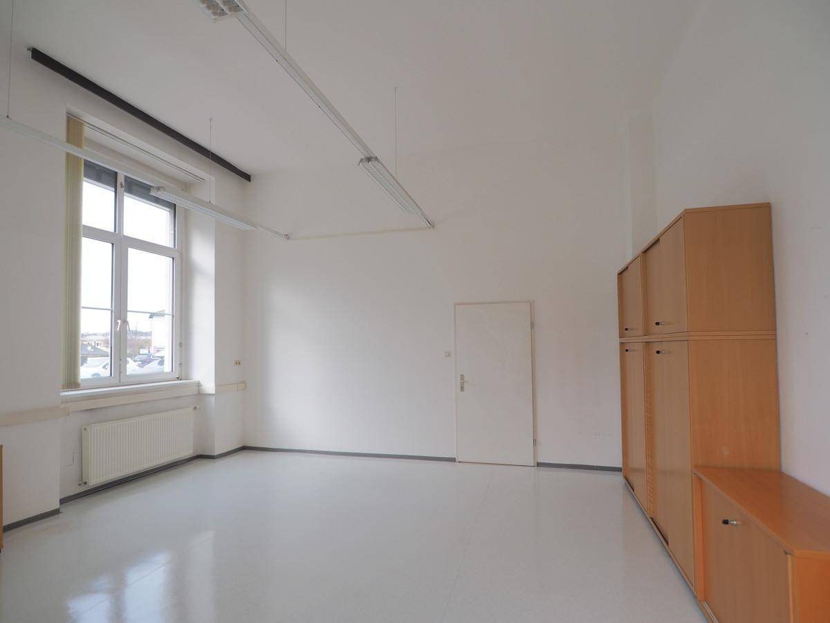 Geräumiger Büroraum mit hellen Wänden, einem großen Fenster und integrierten Holzschränken.