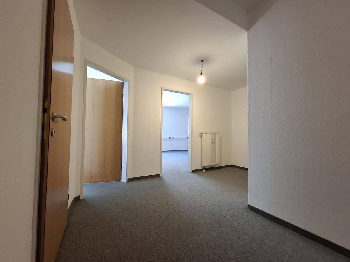 Flur mit grauem Teppichboden, weißen Wänden und mehreren Holztüren, die zu weiteren Räumen führen.