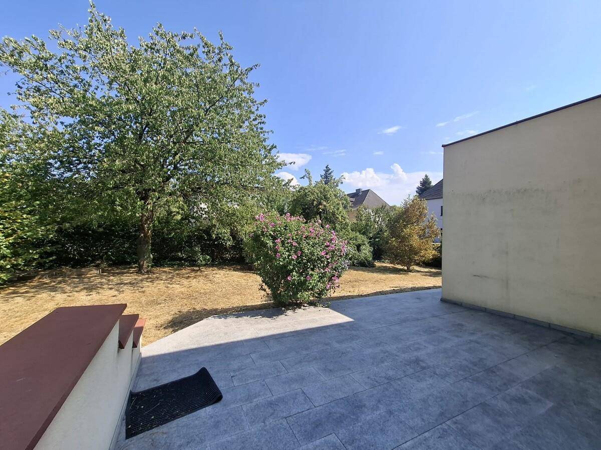 Große gepflasterte Terrasse mit Stufen und Blick auf den grünen Garten.