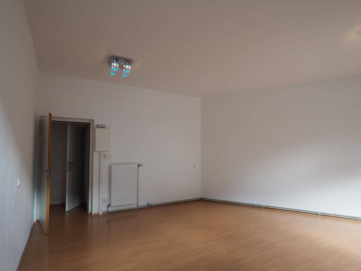 Leerer Gewerberaum mit weiß gestrichenen Wänden, einem Heizkörper und einer Tür zu einem Nebenraum.