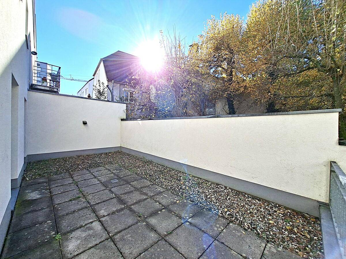 Kleine gepflasterte Terrasse mit Mauern und Blick auf Bäume, ideal für eine Pause im Freien.