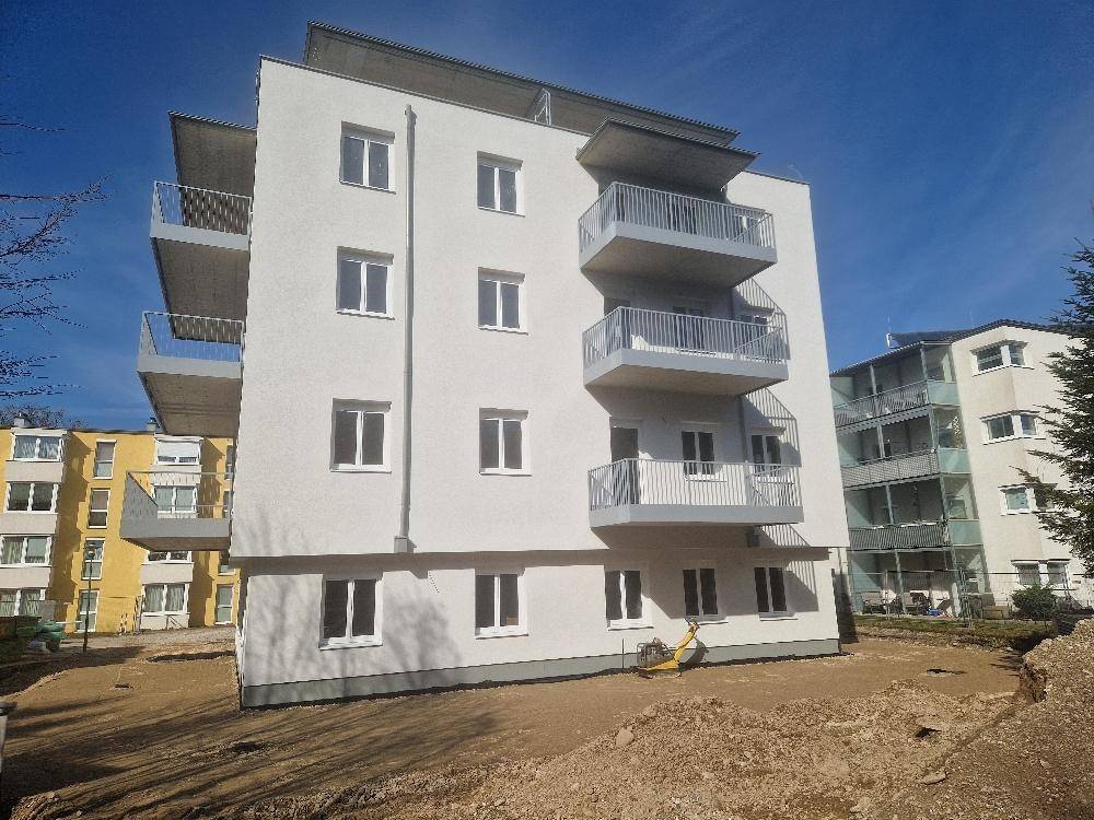 Helle Fassade eines Neubaus mit mehreren Balkonen und großen Fenstern.