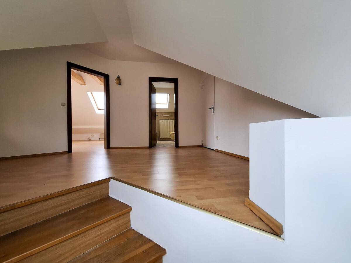 Heller Dachbodenbereich mit Holzparkettboden und Zugang zu weiteren Räumen.
