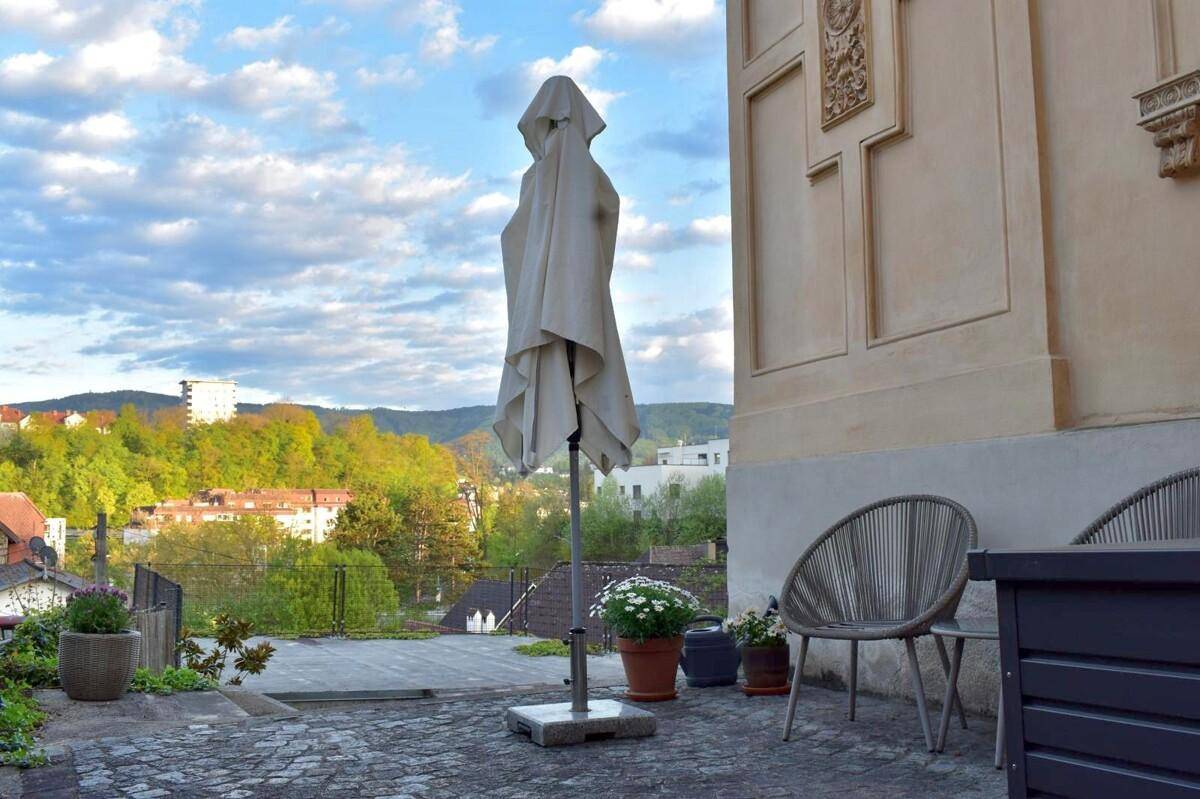 Geräumige Terrasse mit Sitzgelegenheiten, Sonnenschirm und weitem Blick auf die grüne Landschaft und die Stadt.
