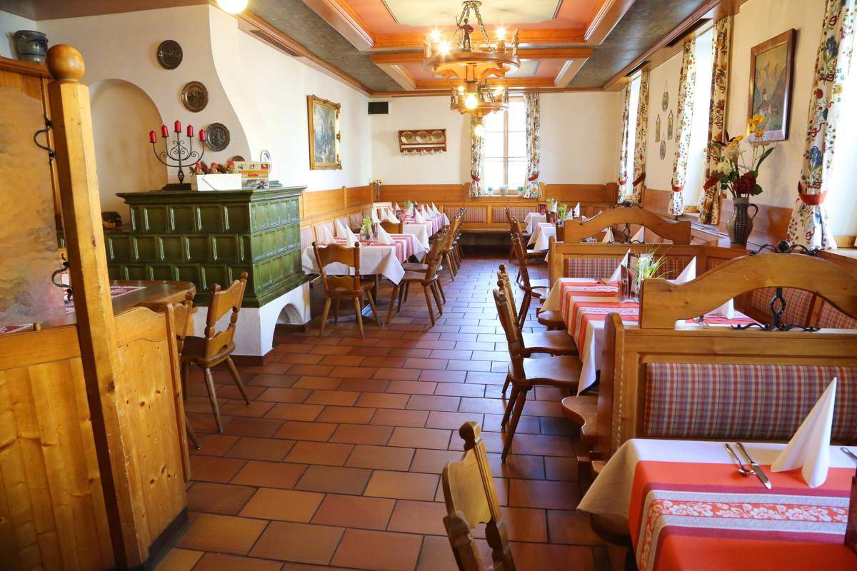 Gemütlicher Speisesaal mit Kachelofen, Holzbänken und traditioneller Einrichtung.