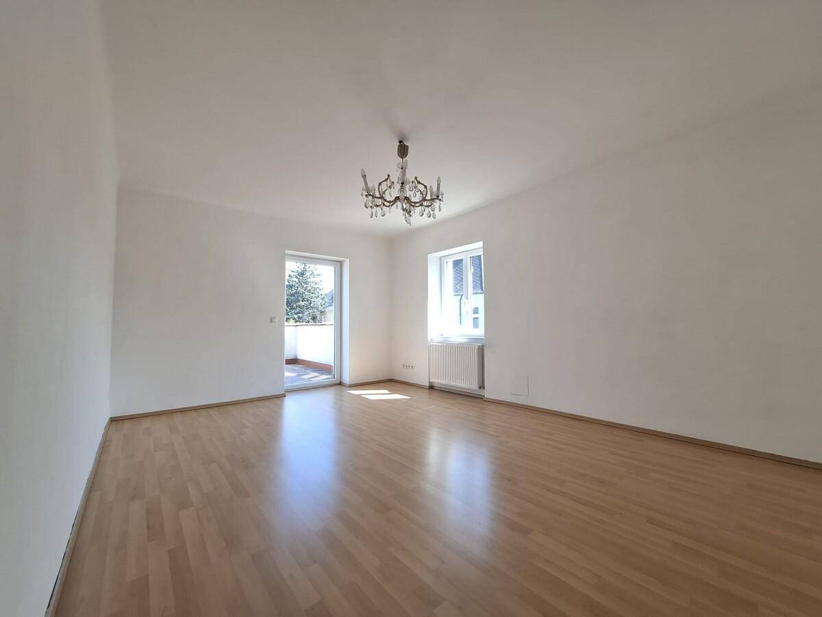 Helles, leeres Zimmer mit Parkettboden, Kronleuchter und Zugang zu einem Balkon.