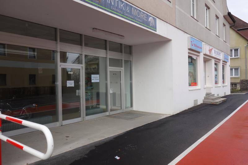 Außenansicht eines Geschäftsgebäudes mit großen Schaufenstern und angrenzendem Gehweg.