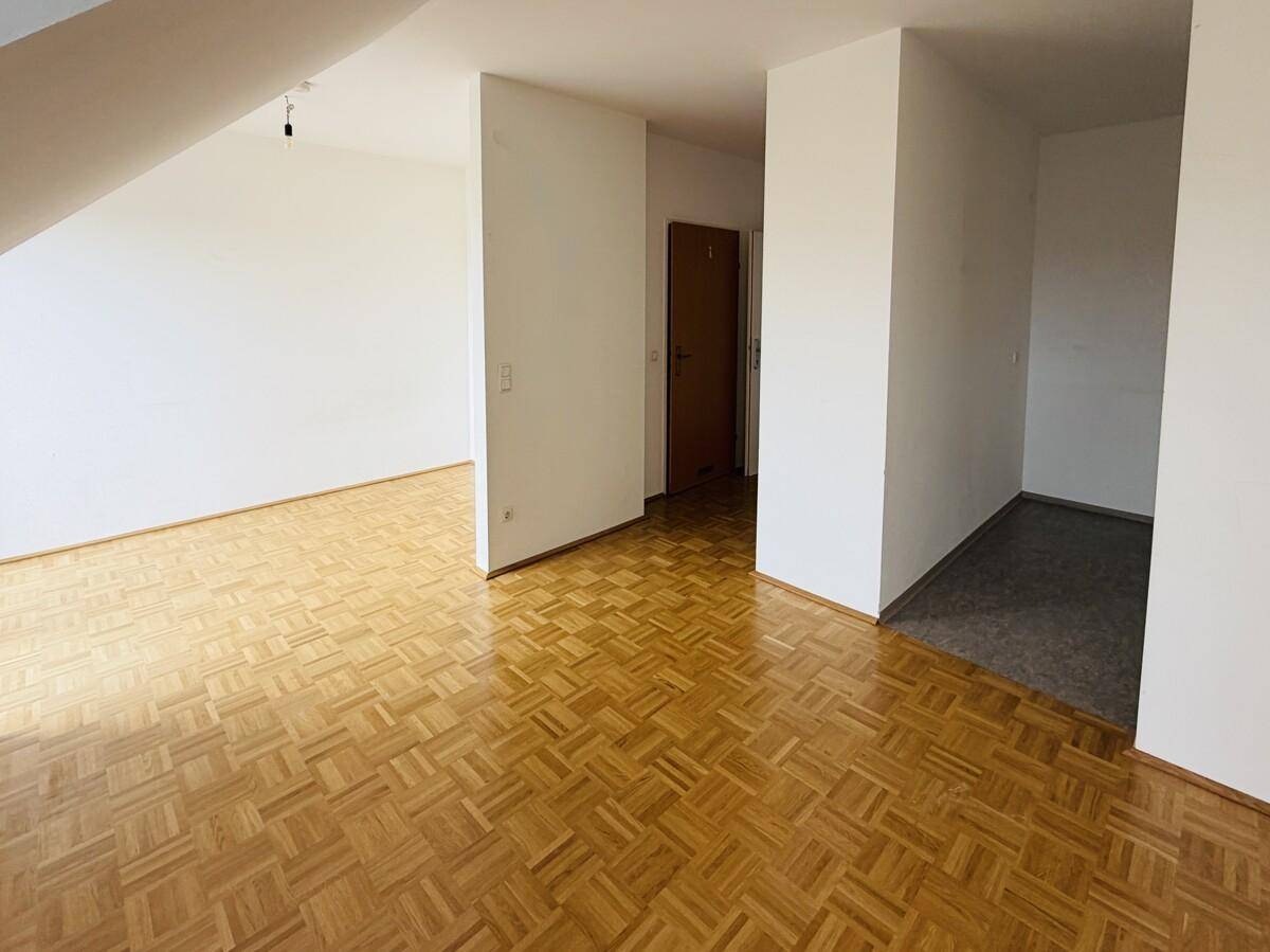 Heller Wohnbereich mit Parkettboden und Übergang zu einem Flur mit dunklen Fliesen.