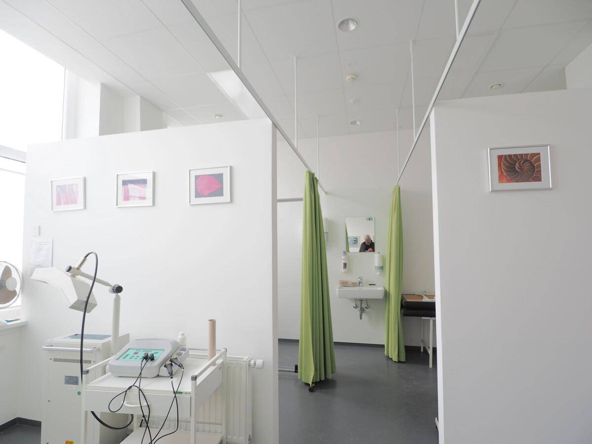 Untersuchungsraum mit medizinischen Geräten, Waschbecken und grünen Vorhängen für Privatsphäre.