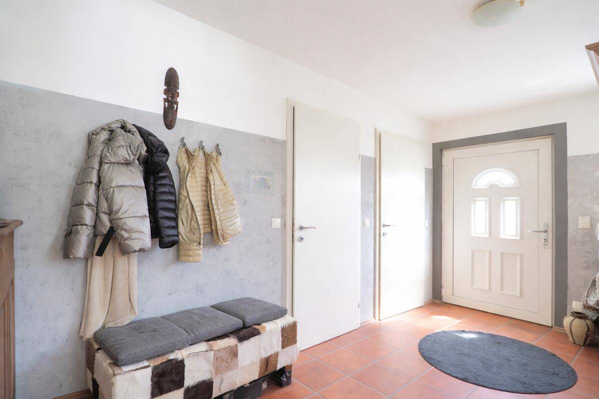Heller Eingangsbereich mit Terrakottafliesen, Garderobe und einer Sitzbank.