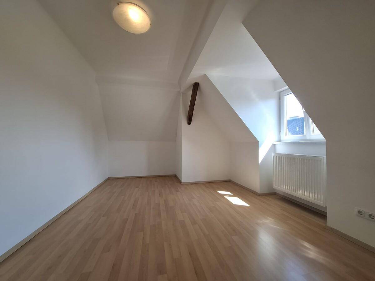 Geräumiges Dachgeschosszimmer mit Parkettboden, Heizkörper und schrägen Wänden.