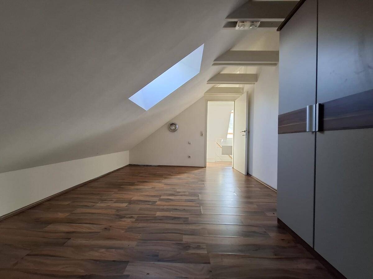 Helles Dachzimmer mit schrägen Wänden, Dachfenster und modernem Laminatboden, ideal als Schlaf- oder Hobbyraum.