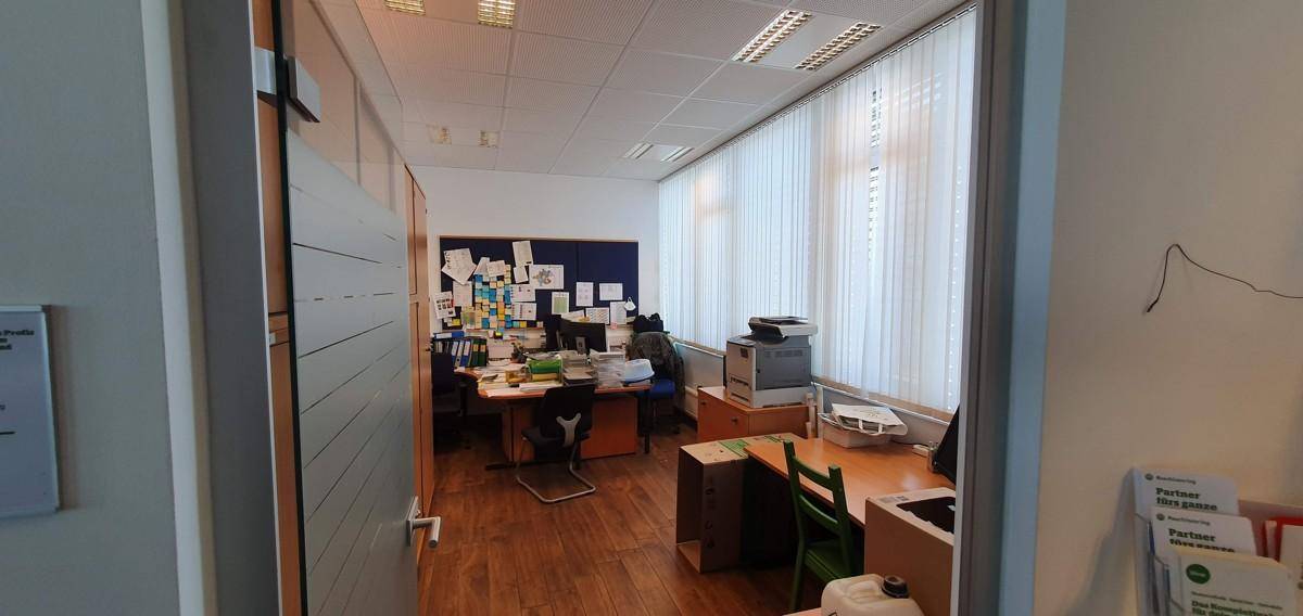 Büro mit Holzboden, großen Fenstern und einem Schreibtischbereich mit Drucker für effizientes Arbeiten.