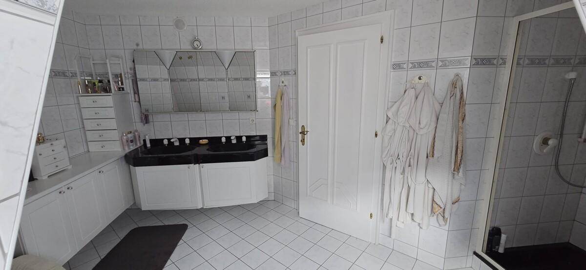 Helles Badezimmer mit weißen Fliesen, Doppelwaschbecken und Duschbereich.