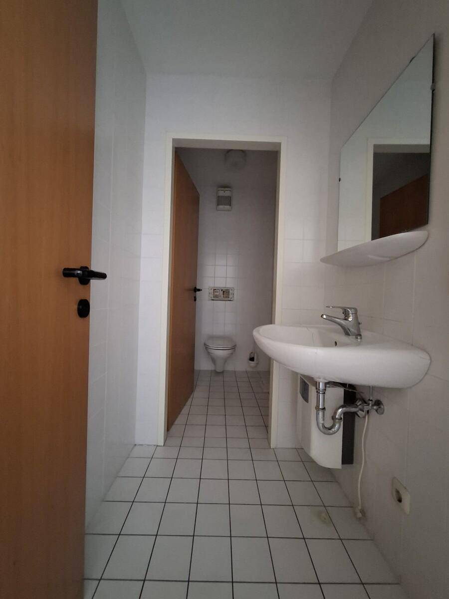 Einfaches Badezimmer mit weißen Fliesen, Waschbecken und Toilette, in gutem Zustand.