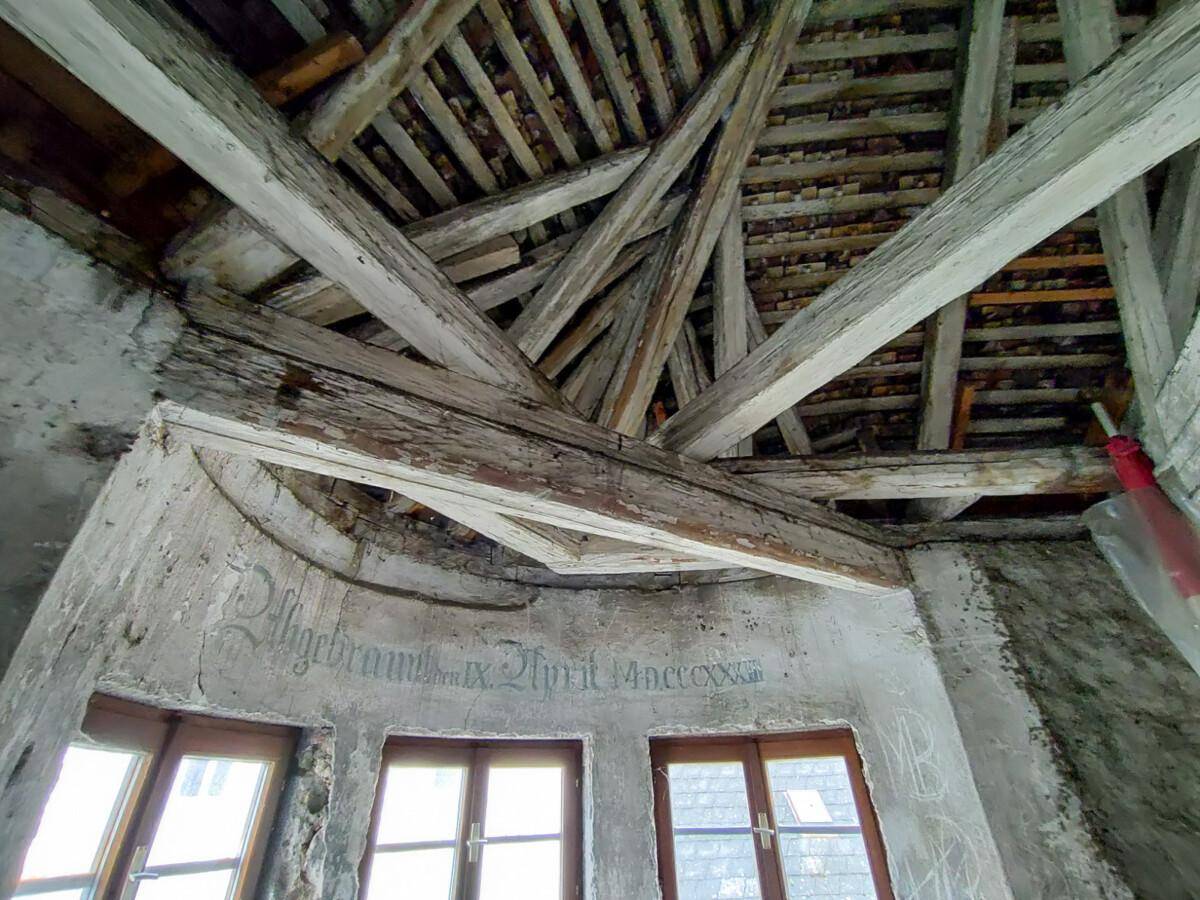 Historische Holzbalkenkonstruktion des Dachstuhls mit sichtbarem Mauerwerk und alten Wandinschriften.